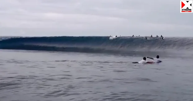 Imagem de uma onda se formando, com surfistas próximos.