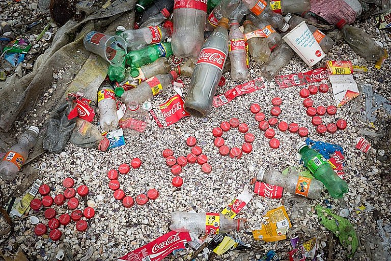 imagem de garrafas de coca- cola em praia ilustra post Coca- cola e plástico no mar
