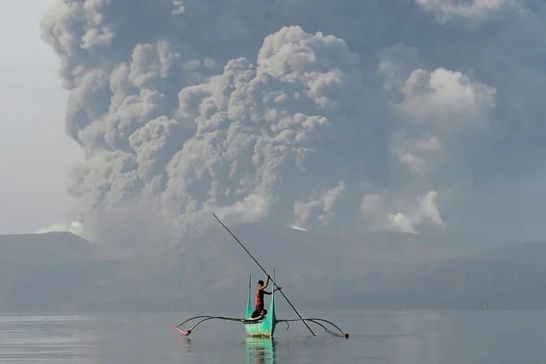 imagem de homem em canoa com vulcão ao fundo