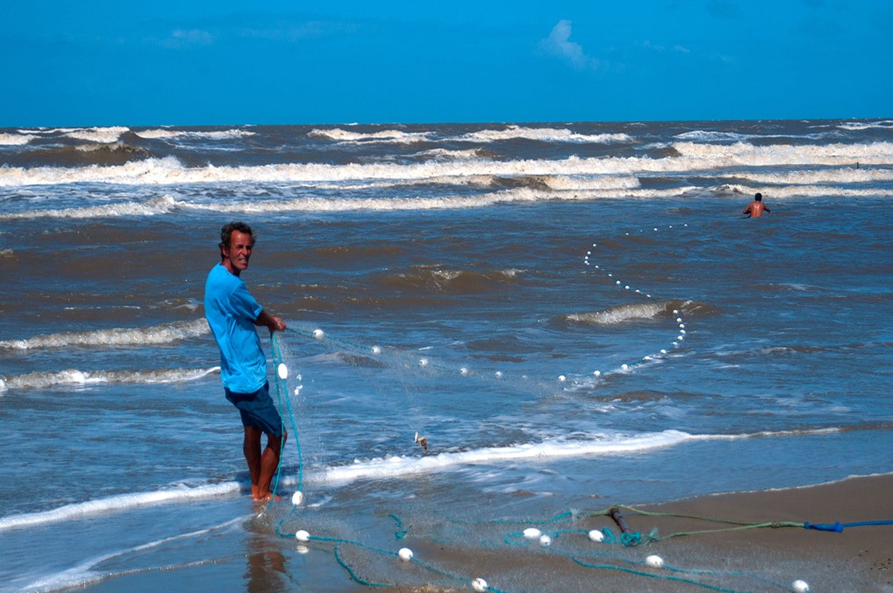 Imagem de pescador passando rede na área de arrebentação